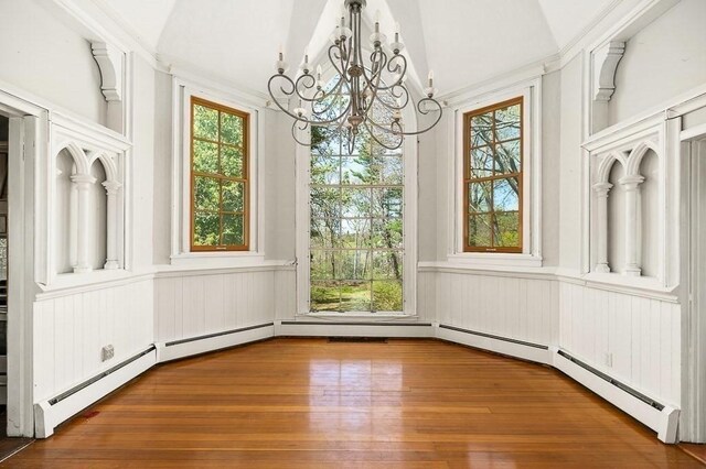 unfurnished dining area with wainscoting, a chandelier, plenty of natural light, wood-type flooring, and vaulted ceiling