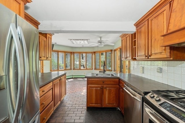 kitchen featuring appliances with stainless steel finishes, a sink, a peninsula, ceiling fan, and dark countertops