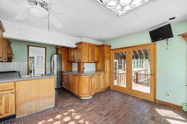 kitchen with freestanding refrigerator, brick patterned flooring, decorative backsplash, ceiling fan, and brown cabinets