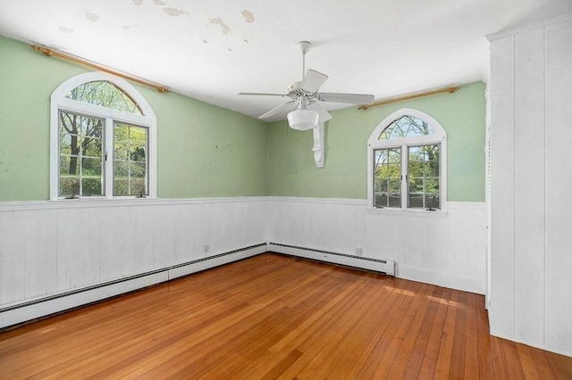 empty room with wainscoting, wood-type flooring, and a ceiling fan