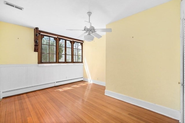 spare room with a baseboard heating unit, ceiling fan, wood finished floors, and baseboards