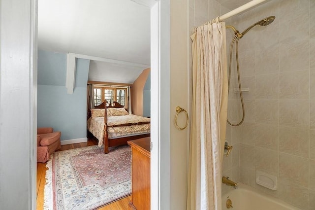 bathroom featuring wood finished floors, vaulted ceiling, ensuite bathroom, shower / bathtub combination with curtain, and baseboards