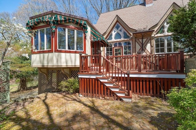 back of house featuring a shingled roof, a deck, and a chimney