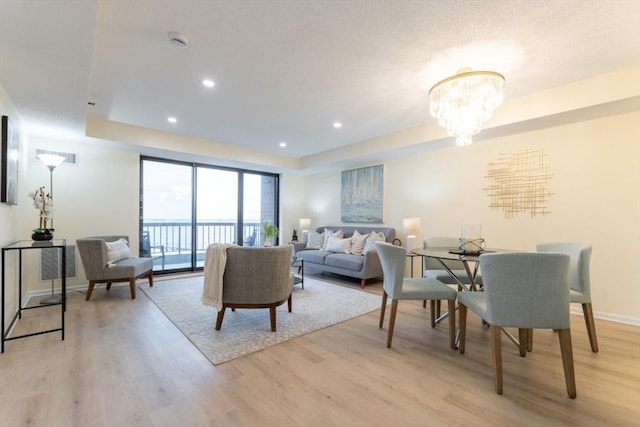 living room with light hardwood / wood-style floors, a raised ceiling, and a chandelier