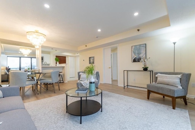 living room featuring a notable chandelier, light wood-type flooring, and a tray ceiling