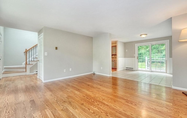 47 Key St Unit 47, Millis, MA 02054 - unfurnished living room featuring light wood-type flooring, stairs, baseboard heating, wainscoting, and a baseboard heating unit