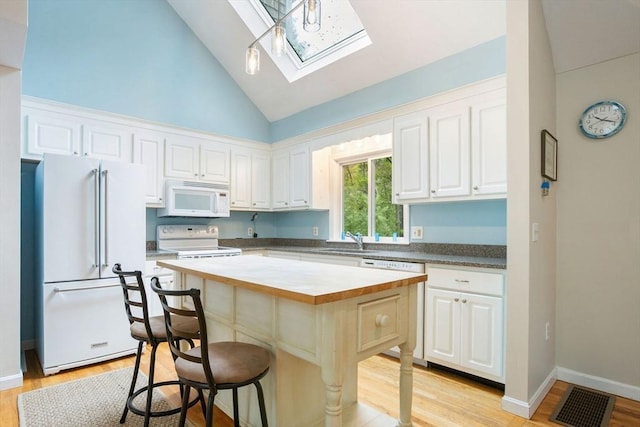 94 Pine View Dr, Brewster, MA 02631 - kitchen featuring white appliances, a skylight, white cabinets, a breakfast bar, and high vaulted ceiling