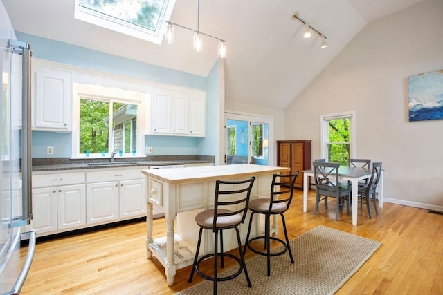 94 Pine View Dr, Brewster, MA 02631 - kitchen with stainless steel fridge, white cabinetry, light wood-style flooring, a skylight, and high vaulted ceiling