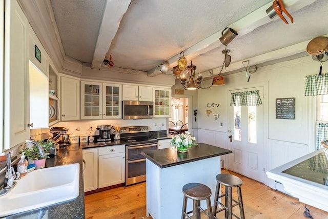 79 Wapping Rd, Kingston, MA 02364 - kitchen with stainless steel appliances, a sink, beamed ceiling, dark countertops, and a breakfast bar