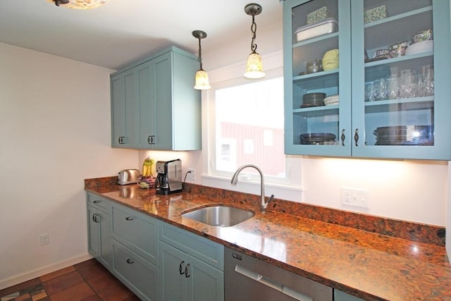 kitchen featuring glass insert cabinets, dark stone countertops, a sink, pendant lighting, and stainless steel dishwasher