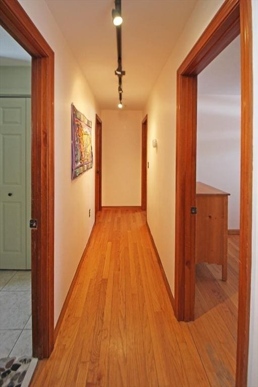 hallway featuring baseboards, rail lighting, and light wood-style floors