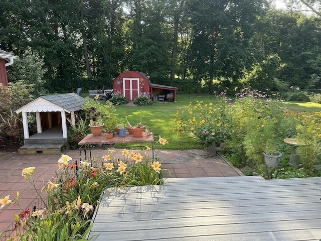 deck with an outdoor structure, a patio area, a yard, and a storage shed