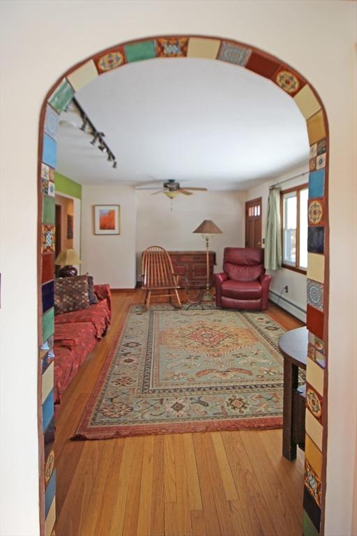 living room with arched walkways, a ceiling fan, wood-type flooring, baseboard heating, and track lighting