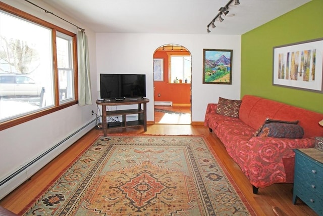 living area featuring arched walkways, baseboard heating, wood finished floors, and rail lighting