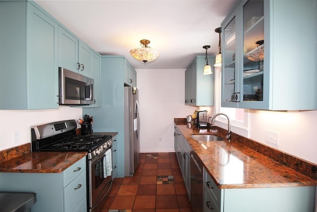 kitchen featuring glass insert cabinets, appliances with stainless steel finishes, dark stone countertops, blue cabinetry, and a sink