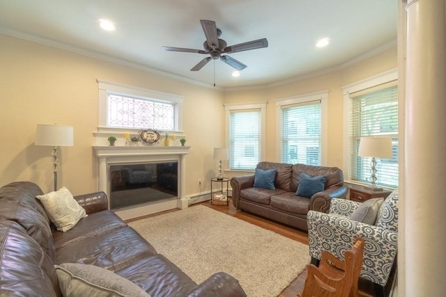 living area featuring ceiling fan, plenty of natural light, a baseboard heating unit, a fireplace with flush hearth, and crown molding