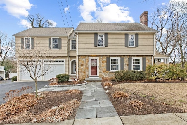 colonial inspired home with aphalt driveway, a garage, stone siding, and a chimney