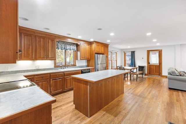 kitchen with sink, black dishwasher, stainless steel fridge, a kitchen island, and light wood-type flooring