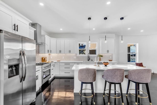 kitchen featuring stainless steel appliances, a sink, wall chimney exhaust hood, a kitchen bar, and backsplash