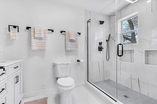 bathroom with a marble finish shower, toilet, vanity, baseboards, and tile patterned flooring