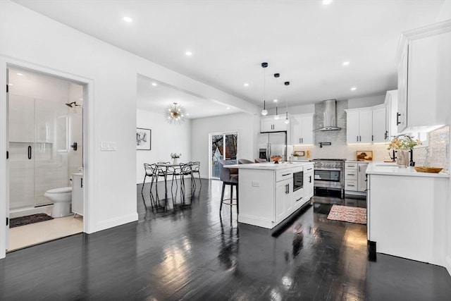 kitchen with wall chimney range hood, stainless steel appliances, dark wood-style floors, a kitchen bar, and white cabinets