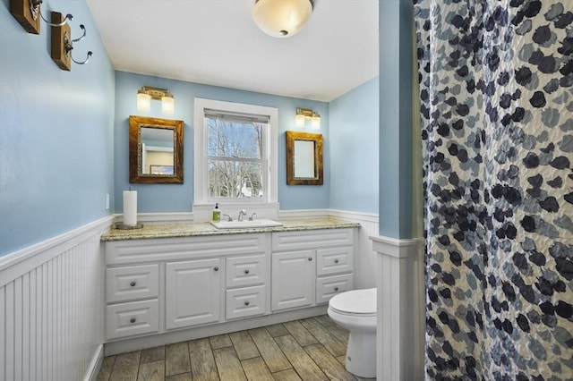 full bathroom with wood finish floors, a wainscoted wall, toilet, and a shower with shower curtain