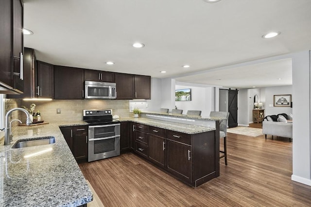 kitchen featuring a breakfast bar, a peninsula, a sink, appliances with stainless steel finishes, and a barn door