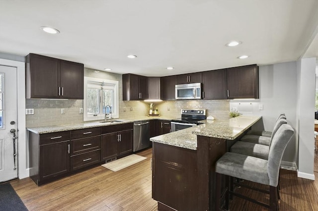 kitchen featuring a peninsula, a sink, dark brown cabinetry, light wood-style floors, and appliances with stainless steel finishes