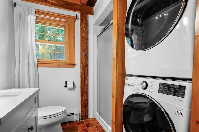 laundry area featuring a baseboard radiator, laundry area, dark tile patterned floors, and stacked washing maching and dryer