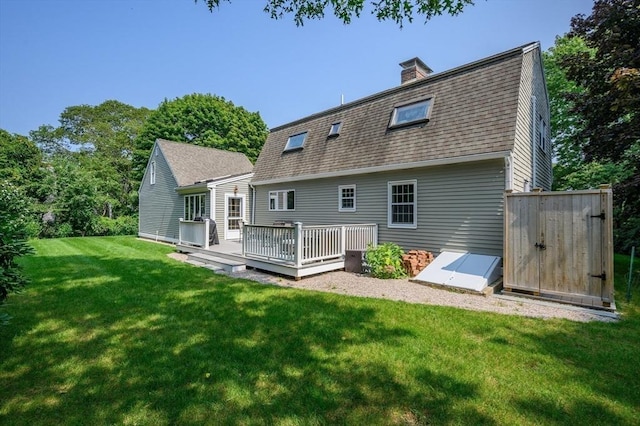 rear view of property with a lawn, a gambrel roof, a chimney, roof with shingles, and a wooden deck