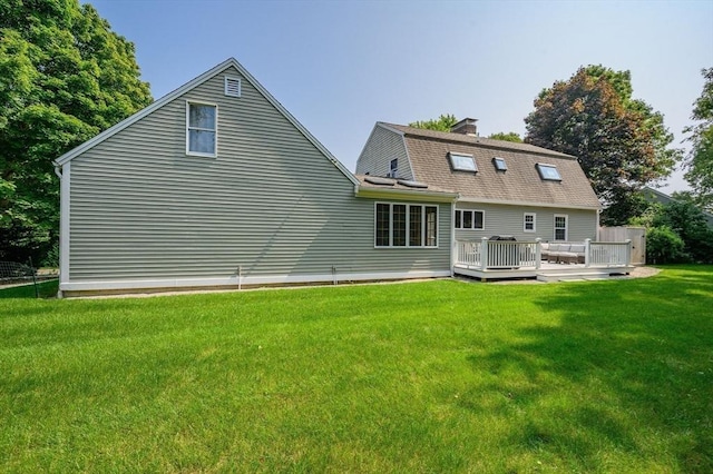 back of property with a lawn, a deck, and a gambrel roof