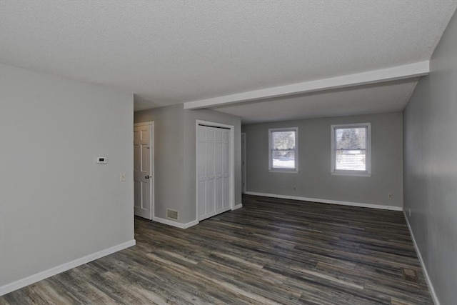 spare room featuring visible vents, a textured ceiling, baseboards, and dark wood-style flooring