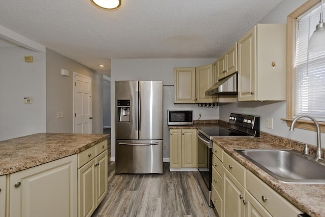 kitchen featuring under cabinet range hood, cream cabinetry, appliances with stainless steel finishes, and a sink