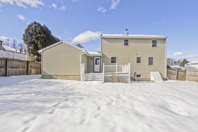 snow covered back of property with a deck and fence