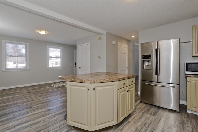 kitchen with cream cabinets, a kitchen island, wood finished floors, stainless steel fridge with ice dispenser, and baseboards