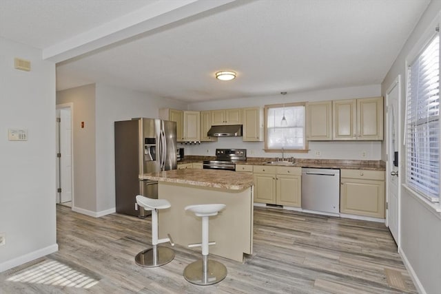 kitchen with under cabinet range hood, a sink, cream cabinets, stainless steel appliances, and light wood-style floors