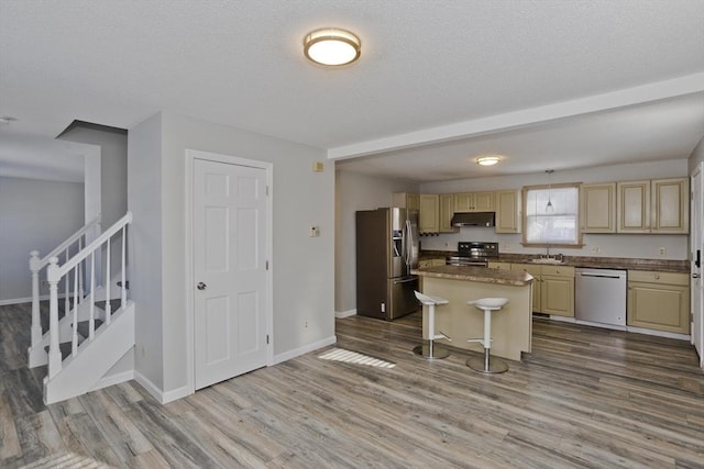 kitchen with wood finished floors, a sink, under cabinet range hood, appliances with stainless steel finishes, and a center island