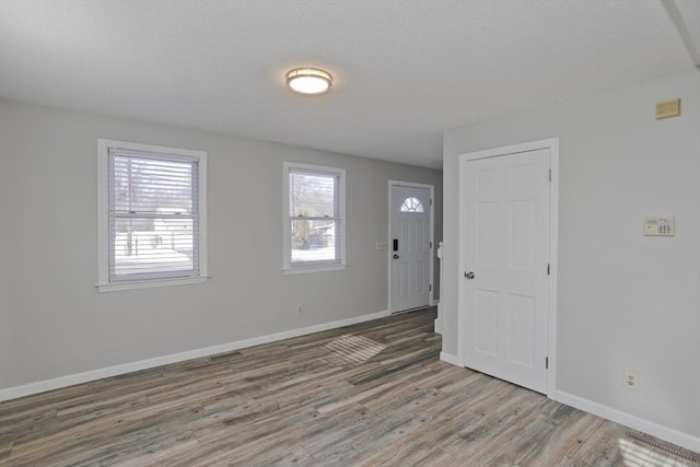 foyer with visible vents, baseboards, a textured ceiling, and wood finished floors