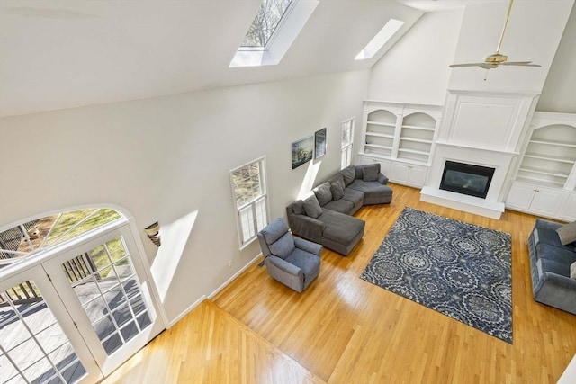 living area featuring built in features, wood finished floors, a skylight, and high vaulted ceiling