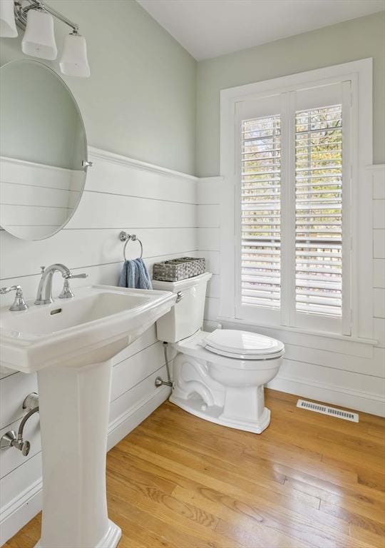 half bath with visible vents, a sink, wood finished floors, and toilet