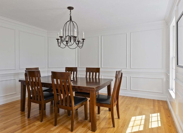 dining area with light wood finished floors, a decorative wall, a chandelier, plenty of natural light, and ornamental molding