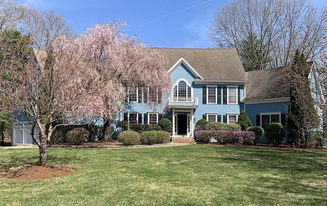 colonial home featuring a balcony and a front yard