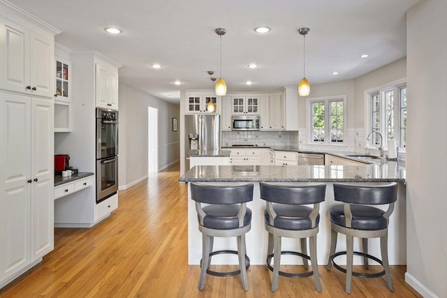 kitchen featuring appliances with stainless steel finishes, tasteful backsplash, a sink, a peninsula, and white cabinetry