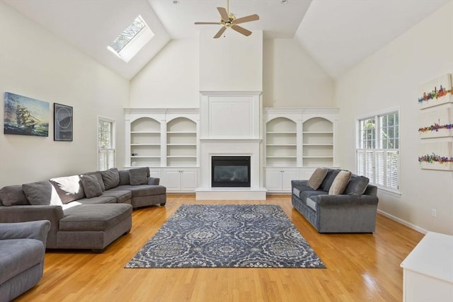 living area with high vaulted ceiling, a skylight, ceiling fan, and light wood-type flooring