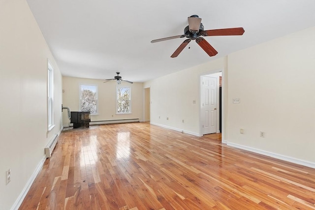 unfurnished living room with baseboard heating, light hardwood / wood-style floors, and a wood stove