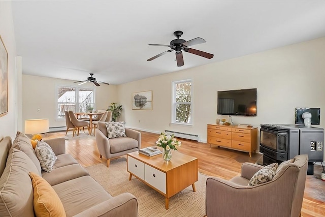 living room with baseboard heating, ceiling fan, light hardwood / wood-style floors, and a wood stove