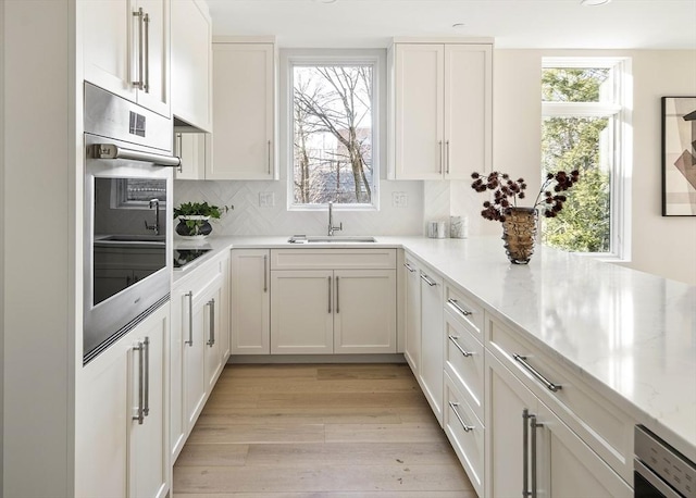 kitchen featuring stainless steel oven, light stone countertops, sink, and white cabinetry