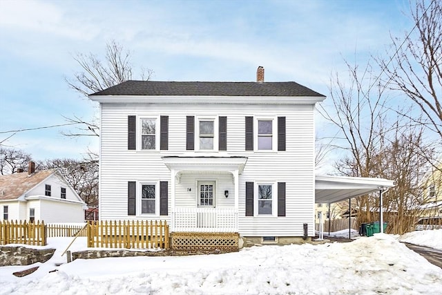 colonial inspired home with roof with shingles, an attached carport, a chimney, and fence