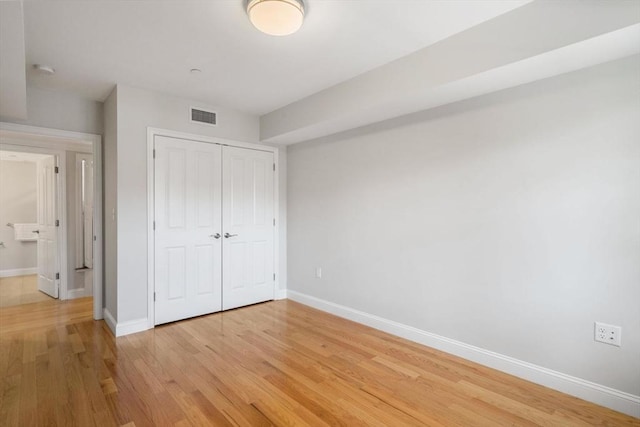 unfurnished bedroom featuring light wood-style floors, a closet, visible vents, and baseboards