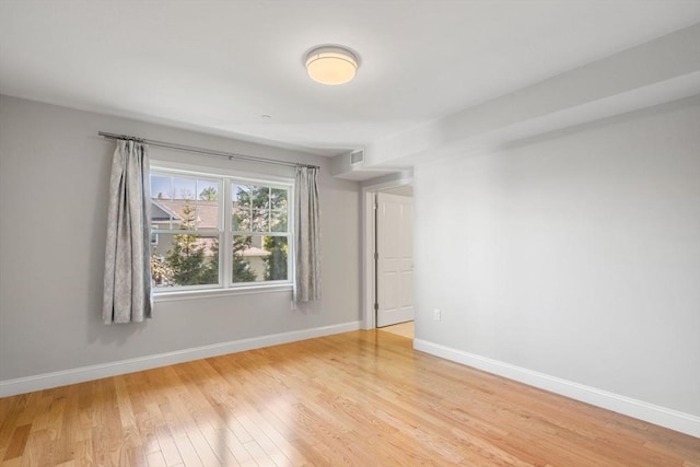 spare room featuring light wood-type flooring, visible vents, and baseboards